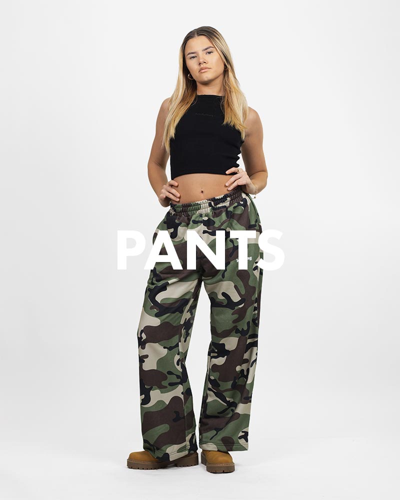 Kobieta w komplecie dresu WASHED CAMO Looking z wyhaftowanym logo Looking, stojąca na białym tle. Na zdjęciu widnieje biały, duży npis PANTS